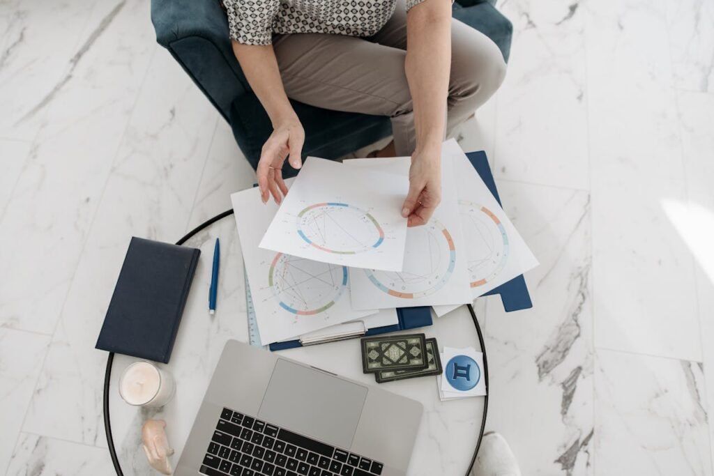 Astrology charts displayed with a laptop, deck of cards, and stationery on a marble floor.