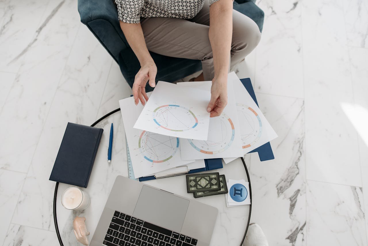 Astrology charts displayed with a laptop, deck of cards, and stationery on a marble floor.